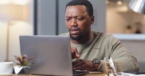 Confused, black man and reading email on laptop with hacker notification update and software fail. Entrepreneur person anxiety, fear and surprise with cyber security breach with information.