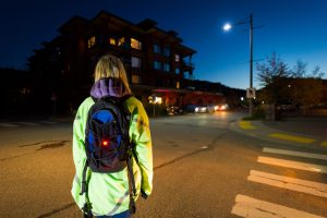 Pedestrian wearing a reflective jacket and wearing a safety light crossing the road at night