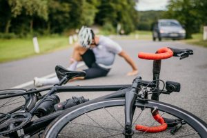 Injured cyclist sitting in pain on the road next to the racing bicycle.