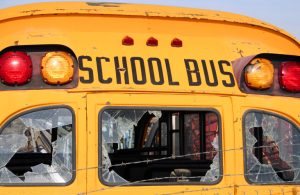 A close-up of the rear of an old school bus with broken windows and rusting paint.