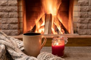 Big mug with hot tea, and a candle , wool scarf, near cozy fireplace, in country house, hygge, home sweet home.