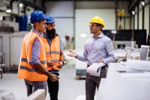 Engineers in factory hall, performing quality control. Manufacturing occupation in modern industrial hall, with automated process and robots. Metal processing industry and warehouse. Employees in factory working together