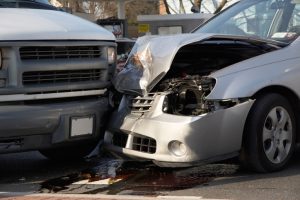 close-up of front end collision between small car and van at a busy intersection.