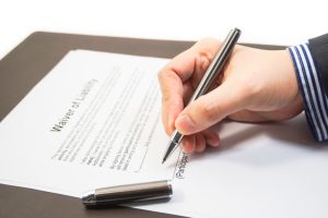 Hand of a businessman signing a waiver form. Signing a waiver of liability form