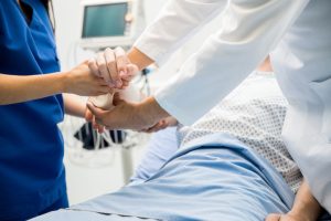 Closeup of the hands of two doctors bandaging a patient's arm in an emergency room