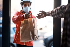 Shot of a masked man delivering a food package. DoorDash. Uber Eats. Grub Hub. Food Delivery Accident. Food delivery driver accident.