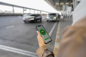 Young muslim woman using mobile app device to order a taxi pick up service by the urban road at airport. Muslim business waiting for uber taxi at outside airport.