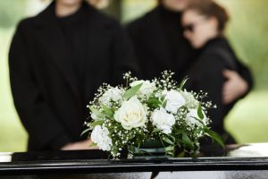 Close up of flower bouquet on coffin with people wearing black in background, outdoor funeral ceremony, copy space. Close up of flower bouquet on coffin.