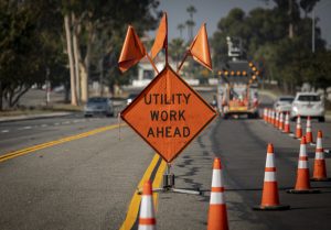 Traffic sign with flags reading Utilitary Work Ahead with traffic cones on road with electronic arrow pointing to the right to divert traffic. Traffic sign with flags reading Utility Work Ahead with traffic cones on road with electronic arrow pointing to the right to divert traffic.